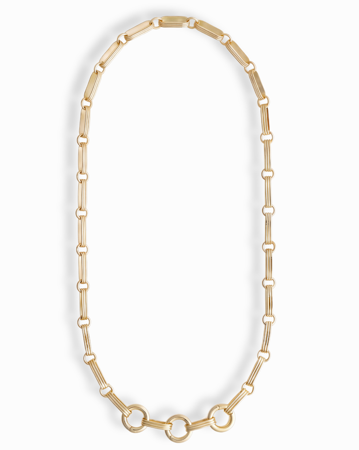 The Jagger Charm Clip Necklace by Mod + Jo features elongated oval links crafted in 14k gold and showcases three larger connected circles at the bottom, elegantly displayed on a white background. This sophisticated necklace seamlessly blends timeless style with contemporary flair.