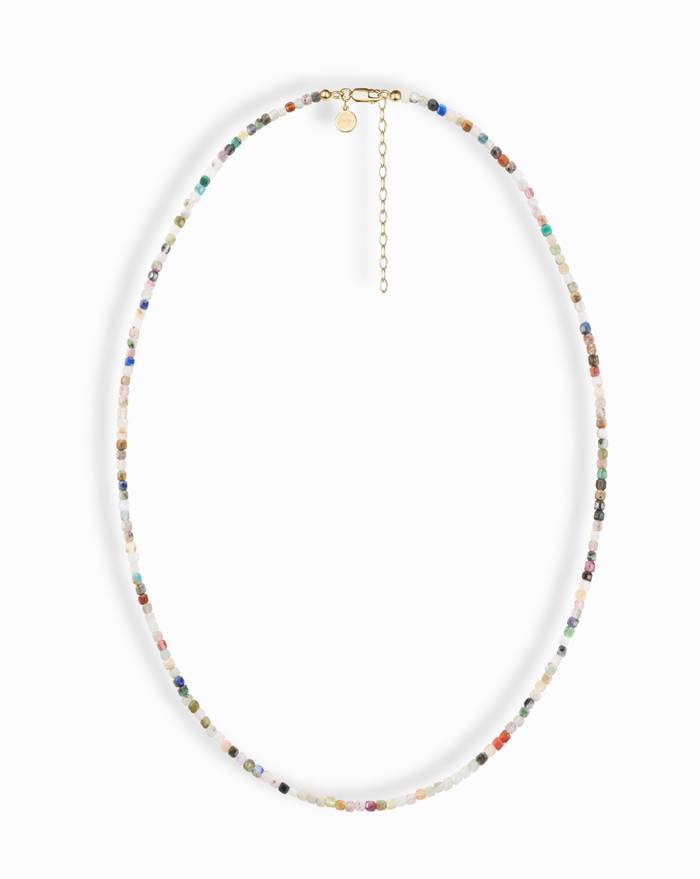 The Mod + Jo Merit Gemstone Necklace features small, multicolored beads, a gold clasp, short extension chain, and round charm. Handmade in Dallas and displayed on a white background.