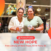 Two women smiling holding colorful mosaic glass lanterns inside a shop with hanging lanterns and window reflections in New Hope, Pennsylvania