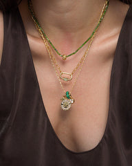 A person wearing Mod + Jo's Nora Lock Carabiner—the luminous, three-layered gold necklace set crafted with 14k plating. One strand is adorned with natural green semi-precious stone beads, another features a refined oval link, and the third showcases a round pendant accented by delicate charms. The look is completed with a deep v-neck brown top.