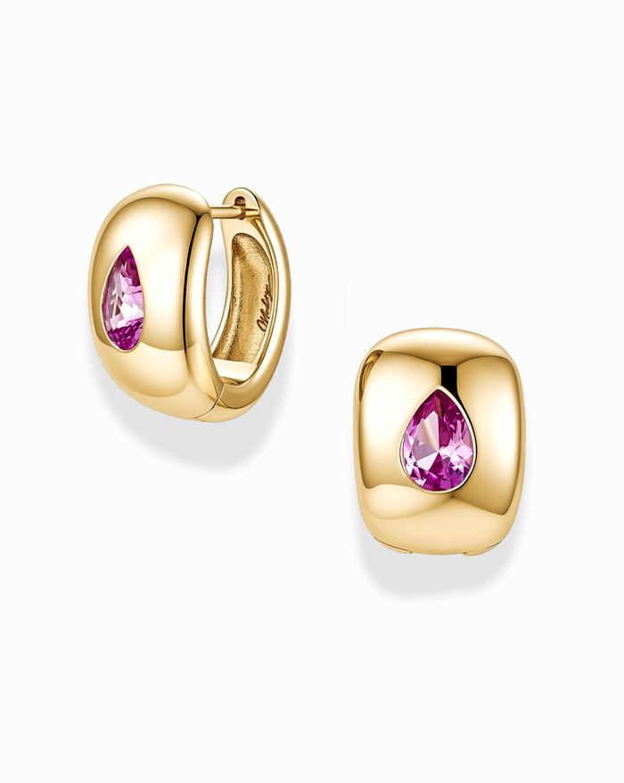 The Mod + Jo Penn Gemstone Hoops are a pair of chunky, gold-plated earrings showcasing a cushion-shaped design with a pink teardrop gemstone at the center and subtle CZ accents. Displayed against a white background, these nickel free hoops bring a bold yet elegant touch to any look.