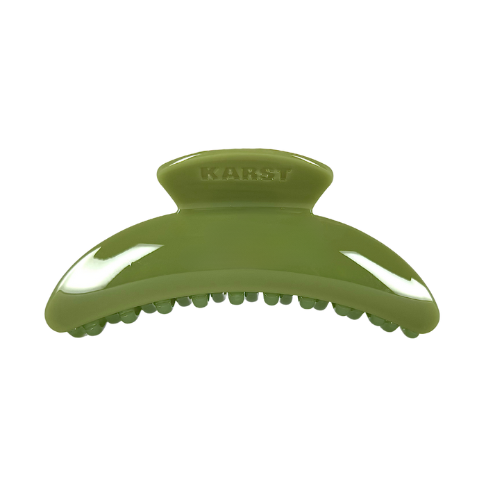The Karst Essentials Slim Hair Claw Clip in olive is a glossy, curved accessory ideal for thicker hair, featuring "KARST" embossed on top and shown against a plain white background.