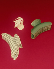 Three SuperClip Hair Claws on a red surface: one small cream, one large green, and one large durable beige and white checkered claw clip.