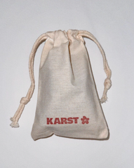 A beige drawstring pouch with "KARST" and a red flower logo on the front, ideal for storing your SuperClip Hair Claw, photographed on a plain white background.