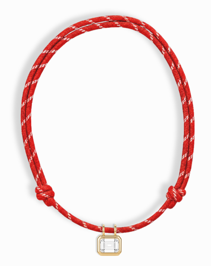 The Mod + Jo Tommy Sapphire Pendant Necklace features two knots on a red and white braided adjustable cord, with a rectangular gold bezel-set pendant showcasing a lab-grown white sapphire at the center.