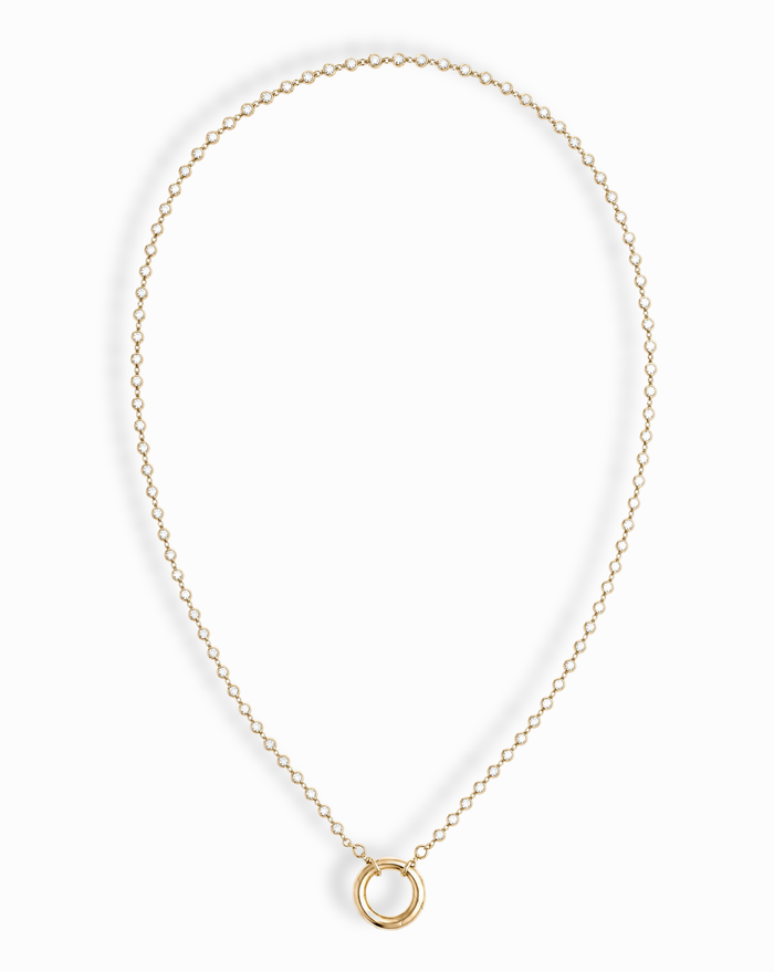 The Callum Tennis Charm Clip Necklace by Mod + Jo features a dainty gold-plated chain with a small circular pendant, elegantly displayed on a white background.