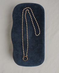 The Mod + Jo Callum Tennis Charm Clip Necklace, featuring a circular pendant and gold plating, is displayed atop a dark blue, velvet-textured case on a light surface.