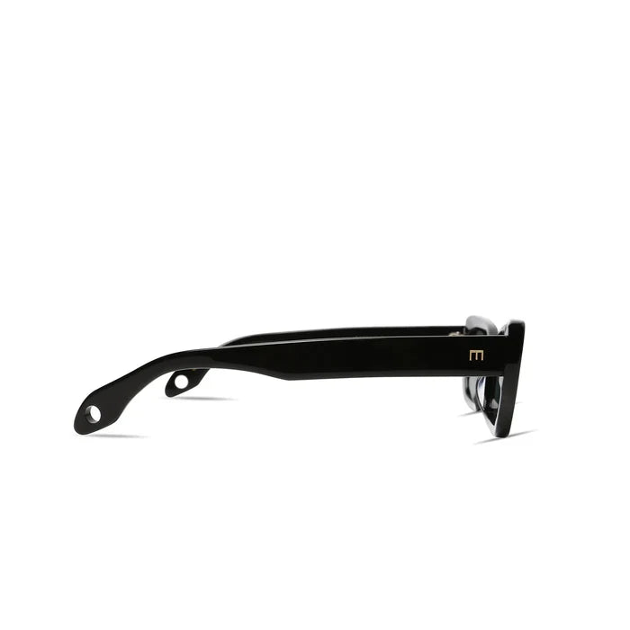 Side view of black Cookie Sunglasses by Elisa Johnson, crafted from acetate with thick arms, a small gold "m" logo near the hinge, and rounded holes at each arm’s end. These cat-eye frames provide stylish UV400 protection against a white background.