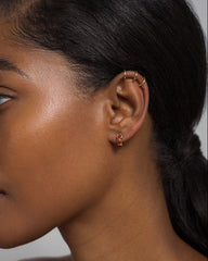 Close-up of a woman's left ear wearing Mod + Jo's Corynn Gemstone Huggies—three 18k gold plated hoops and a small stud with natural red agate. Her dark hair is pulled back, highlighting her smooth, radiant skin.