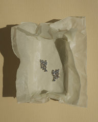 A pair of Mod + Jo Gabby Marquise Dangle Studs, featuring small, silver, flower-shaped cubic zirconia settings, rests on crumpled tissue paper against a textured, pale yellow background.