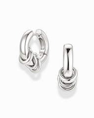The Mod + Jo Grande Levi Huggies are a pair of shiny silver, rhodium plated statement earrings, each featuring three small interlocking rings at the bottom. Displayed on a plain white background, these modern huggie earrings add a touch of elegance to any look.