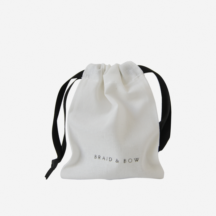 A small white drawstring bag with black ribbon ties securely holds your Large Chocolate Brown Hair Claw. The bag features BRAID & BOW printed in gray text on the front, set against a plain white background.