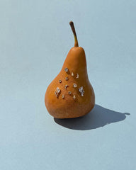 A brown pear stands upright on a light blue background, its front adorned with small, shiny charms shaped like stars, moons, and circles, reminiscent of the delicate gold plating of Mod + Jo’s Libbie Puffy Star Studs.