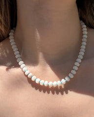 A close-up of a person’s neck wearing the Mod + Jo Macey Gemstone Necklace, featuring round, light blue and white translucent jade stones, with natural lighting highlighting the genuine gems and skin.