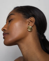 A woman with smooth brown skin and dark hair in a low ponytail tilts her head back, eyes closed, highlighting Mod + Jo’s Milley Spiral Statement Studs against a plain light background.