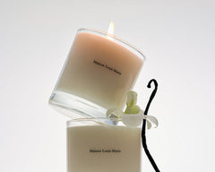 Two Maison Louis Marie candles with an orchid and vanilla bean on a white background