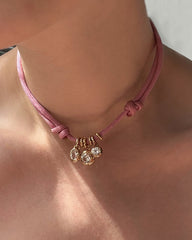 A close-up of a person wearing Mod + Jo’s pink cord choker, featuring three Olly Sapphire Bezel Charms—each set with a clear, round lab-grown white sapphire in 14k gold—against bare skin.