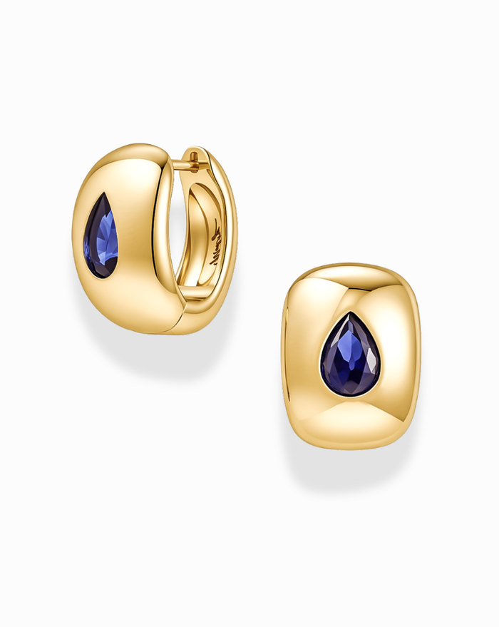 A pair of Mod + Jo Penn Gemstone Hoops in gold plated brass, designed in a rounded square huggie style and set with a teardrop-shaped blue gemstone at the center, accented by delicate CZ stones. Shown on a white background, these nickel-free earrings offer comfortable wear.