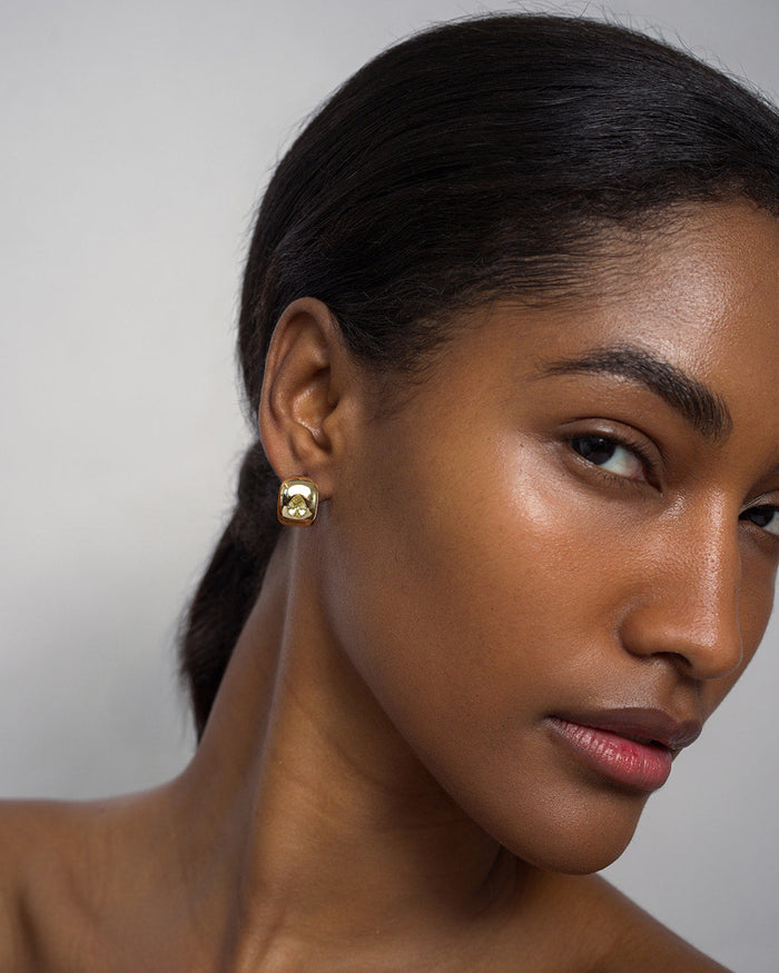 A woman with smooth skin and dark hair pulled back wears the Mod + Jo Penn Gemstone Hoops, featuring lustrous gold plating over brass. She has a neutral expression and is photographed against a plain light background.