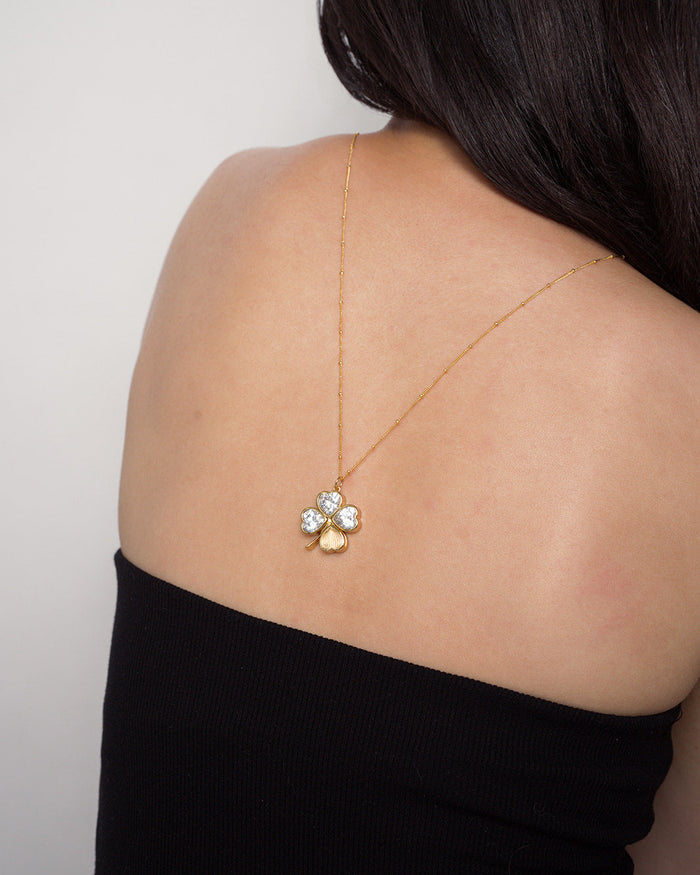 A woman with long dark hair wears the Mod + Jo Perry Four-Leaf Clover Locket Charm necklace, draped down her bare back above a black, strapless top.
