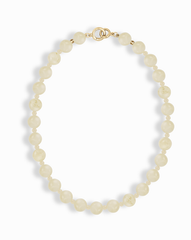 The Portia Gemstone Necklace by Mod + Jo features round, off-white pearl beads and a 14k gold-plated clasp, arranged in an oval shape on a white background.