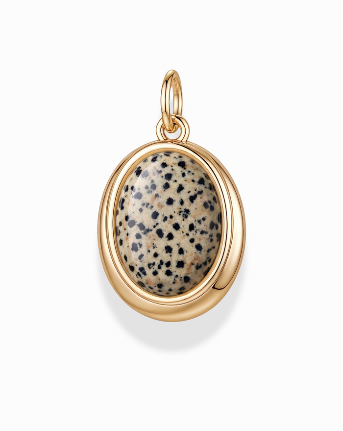 The Rory Gemstone Charm by Mod + Jo features an oval polished Dalmatian Jasper stone with a beige base and black spots, set in a smooth 14k gold over brass bezel with a top loop for easy attachment to a necklace.