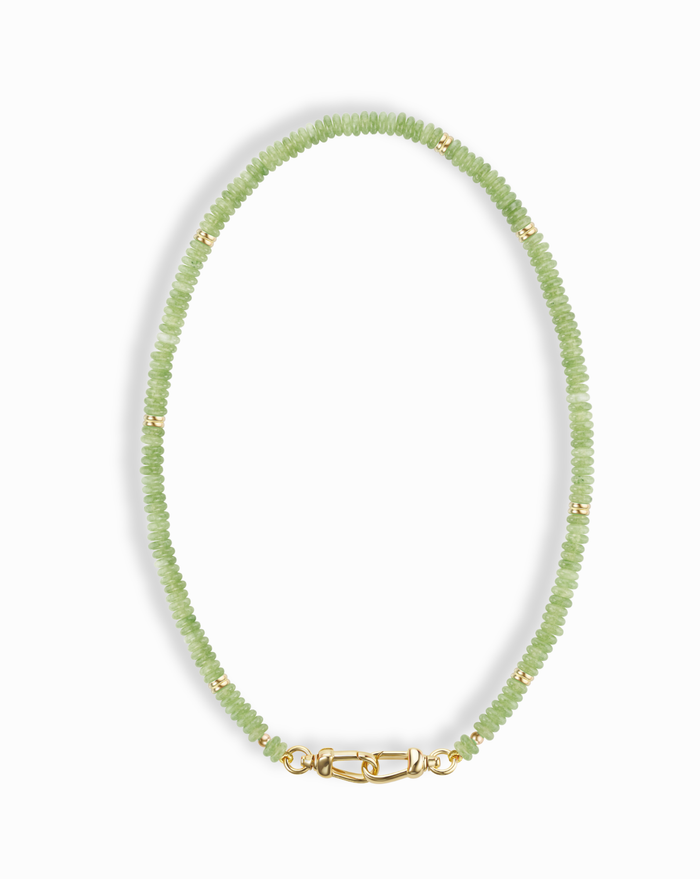 The Sonia Gemstone Necklace by Mod + Jo features small, round, light green genuine gemstone beads with gold spacers and a gold clasp, elegantly arranged in an oval shape against a white background.
