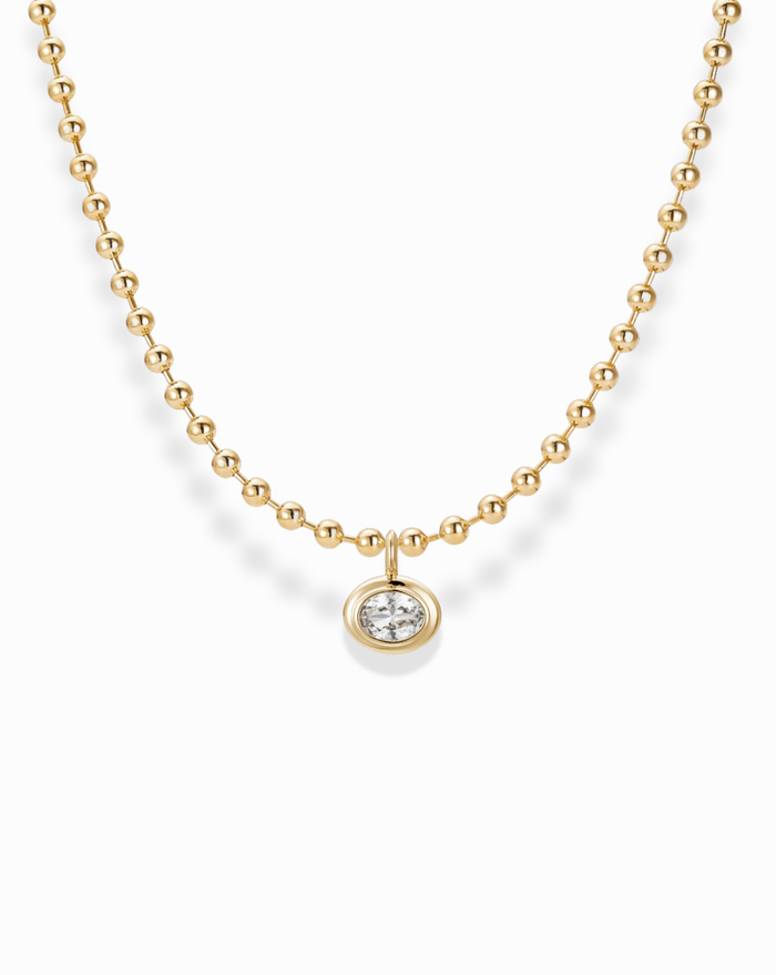 The Soren Bezel Pendant Necklace by Mod + Jo is a 14k gold plated, nickel-free beaded necklace with a round lab-grown white sapphire pendant, shown on a white background.