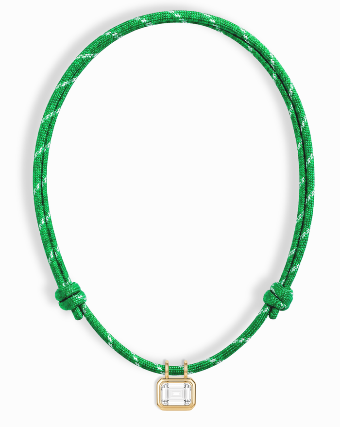 The Mod + Jo Tommy Sapphire Pendant Necklace features a green adjustable paracord with white accents and a rectangular lab-grown white sapphire set in a gold frame at the center.
