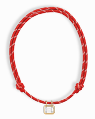 The Mod + Jo Tommy Sapphire Pendant Necklace features two knots on a red and white braided adjustable cord, with a rectangular gold bezel-set pendant showcasing a lab-grown white sapphire at the center.
