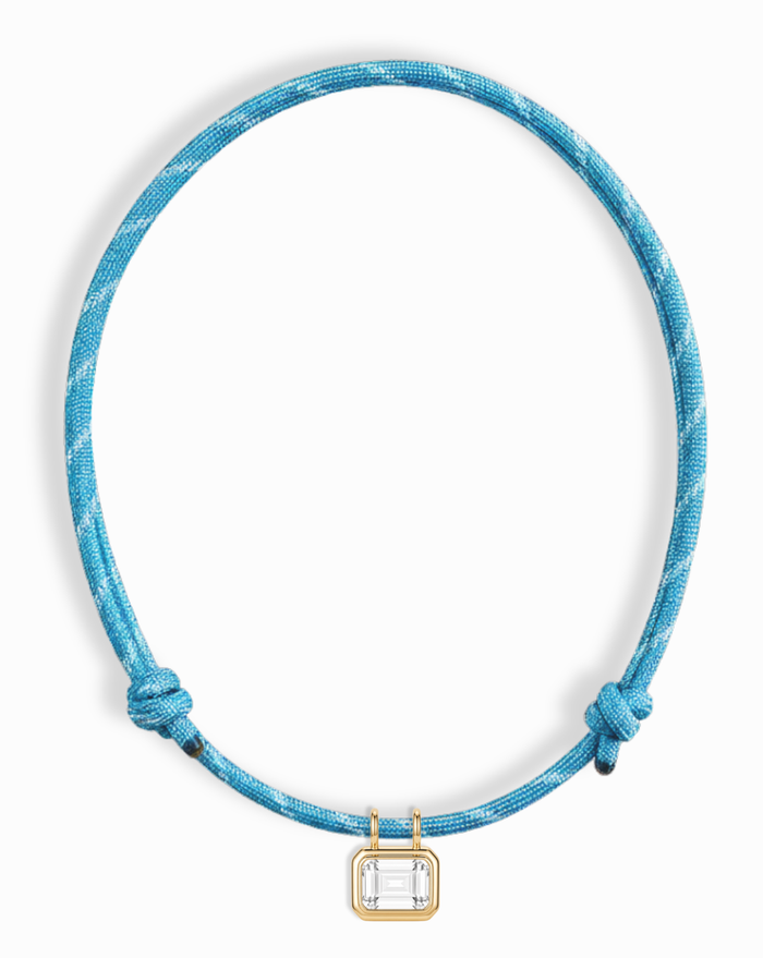 The Mod + Jo Tommy Sapphire Pendant Necklace features a blue cord with two adjustable knots and a gold bezel-set, lab-grown rectangular white sapphire at the center.