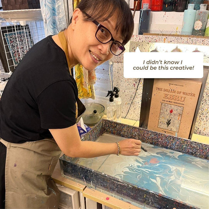 Woman creating marbled art with water and paint in an art studio, expressing creativity